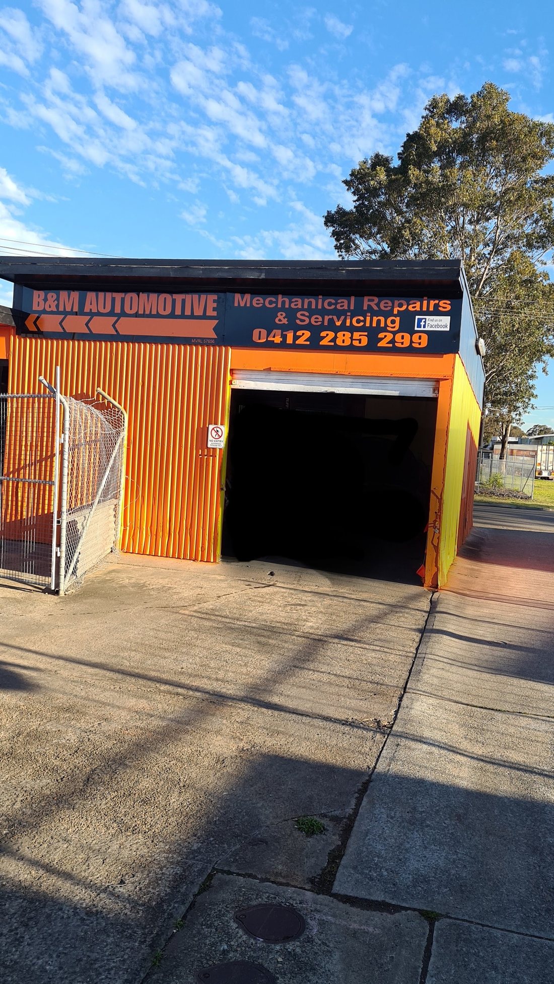 B&M Automotive signage above an open roller door, with the phone number 0412 285 299